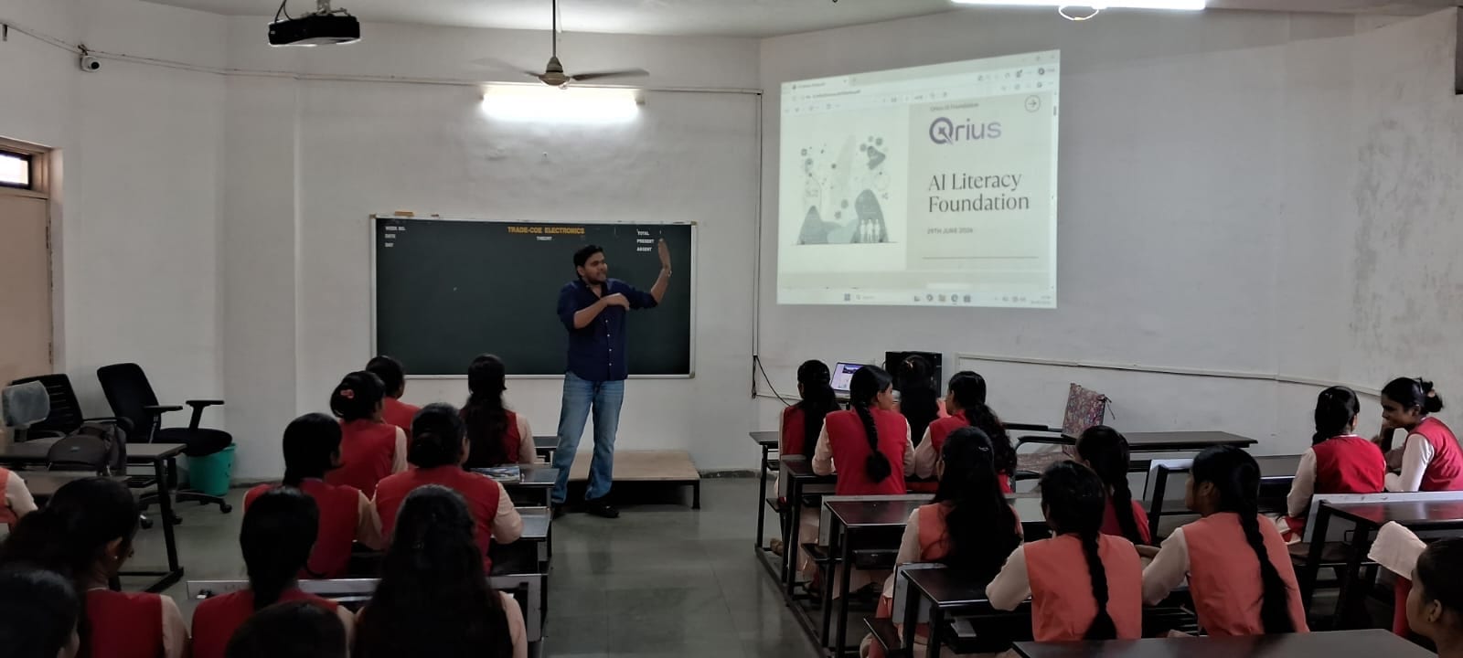 A facilitator presenting AI literacy fundamentals to a classroom of students, with a QriusAI-branded slide on screen.